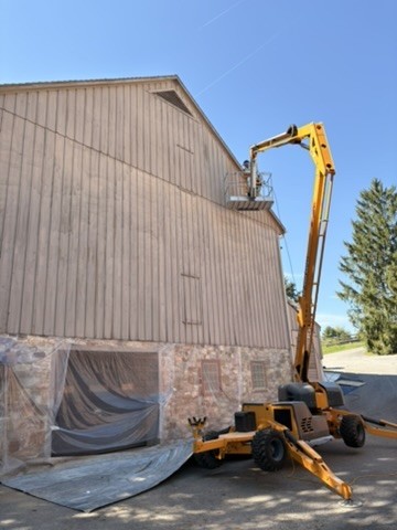 SB Painting crew using a lift to paint the tall gable of the home, with windows covered in plastic